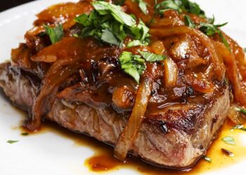 Bifes de cebolada tradicionais com molho rico e cebola caramelizada servidos numa frigideira portuguesa.