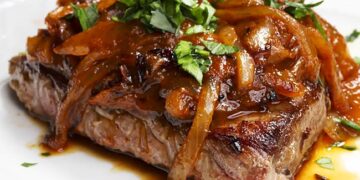 Bifes de cebolada tradicionais com molho rico e cebola caramelizada servidos numa frigideira portuguesa.