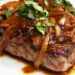 Bifes de cebolada tradicionais com molho rico e cebola caramelizada servidos numa frigideira portuguesa.