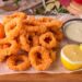 Aprenda a fazer Calamares Fritos à Andaluza! Deliciosos anéis de lula macios e crocantes, fritos com perfeição e servidos com uma pitada de limão.