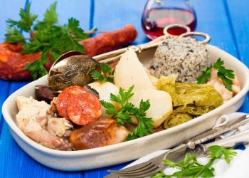 Prato tradicional de Cozido à Portuguesa com carnes, enchidos, legumes e arroz numa travessa.