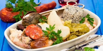 Prato tradicional de Cozido à Portuguesa com carnes, enchidos, legumes e arroz numa travessa.