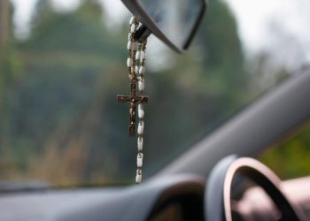 terço e ambientador pendurados no retrovisor de um carro