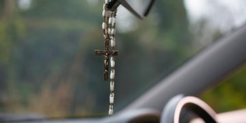 terço e ambientador pendurados no retrovisor de um carro