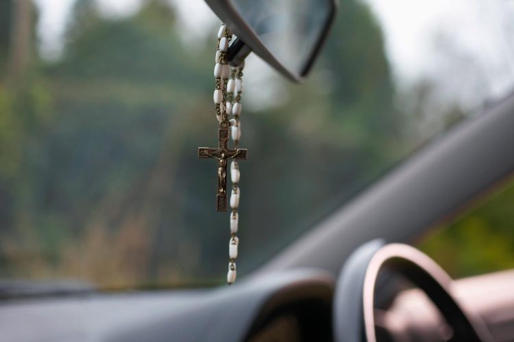 terço e ambientador pendurados no retrovisor de um carro