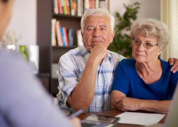 idoso a analisar documentos de reforma e cálculos financeiros em casa