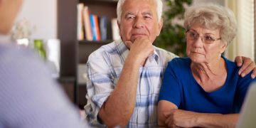 idoso a analisar documentos de reforma e cálculos financeiros em casa