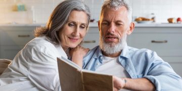 casal sénior feliz a caminhar na praia ao pôr do sol simbolizando reforma antecipada